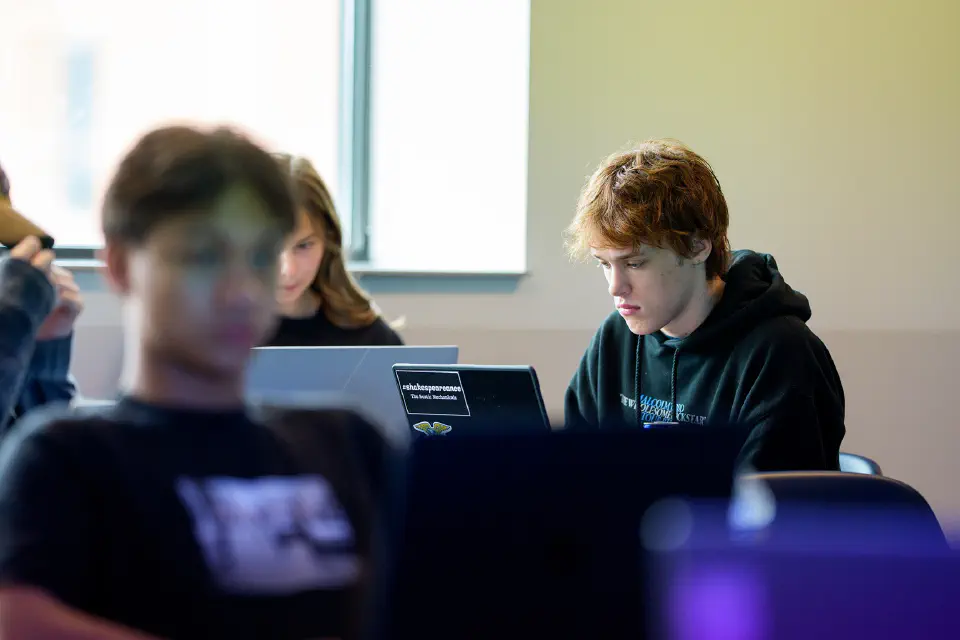a group of students focused on their laptops in what appears to be a classroom or study environment.